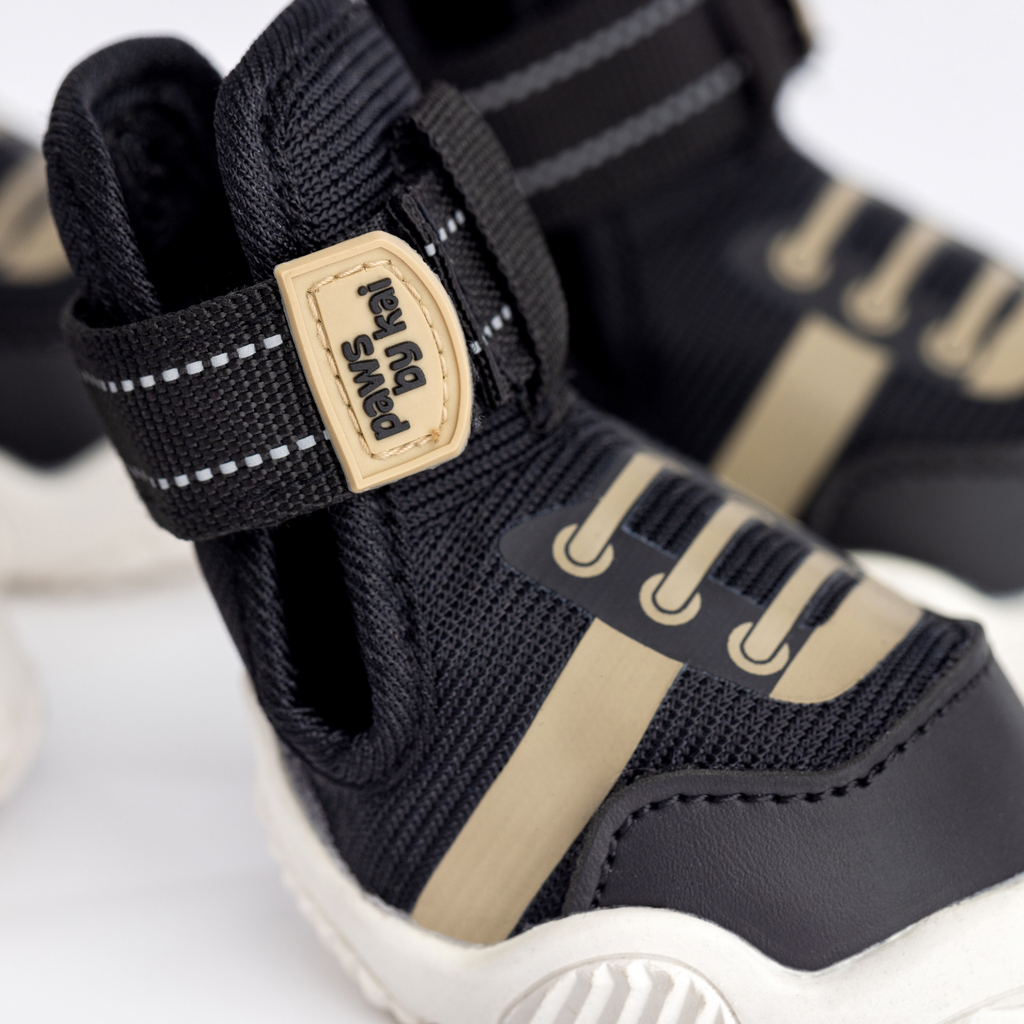 Close-up of black dog sneaker with beige logo patch and hook-and-loop strap
