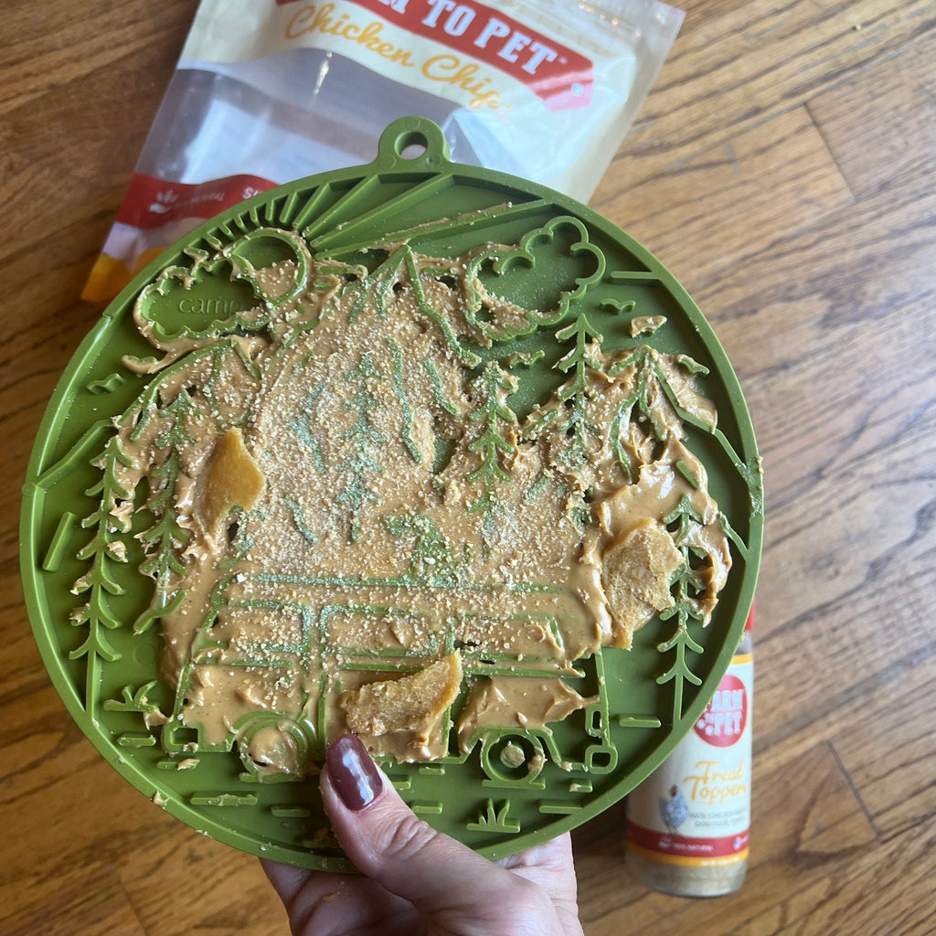 Green dog lick mat with forest pattern, filled with thick creamy treat in hand.