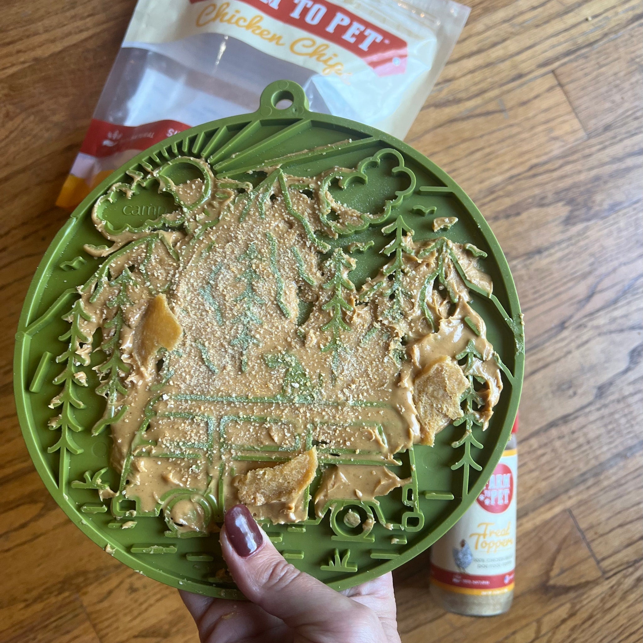 Green dog lick mat with forest pattern, filled with thick creamy treat in hand.