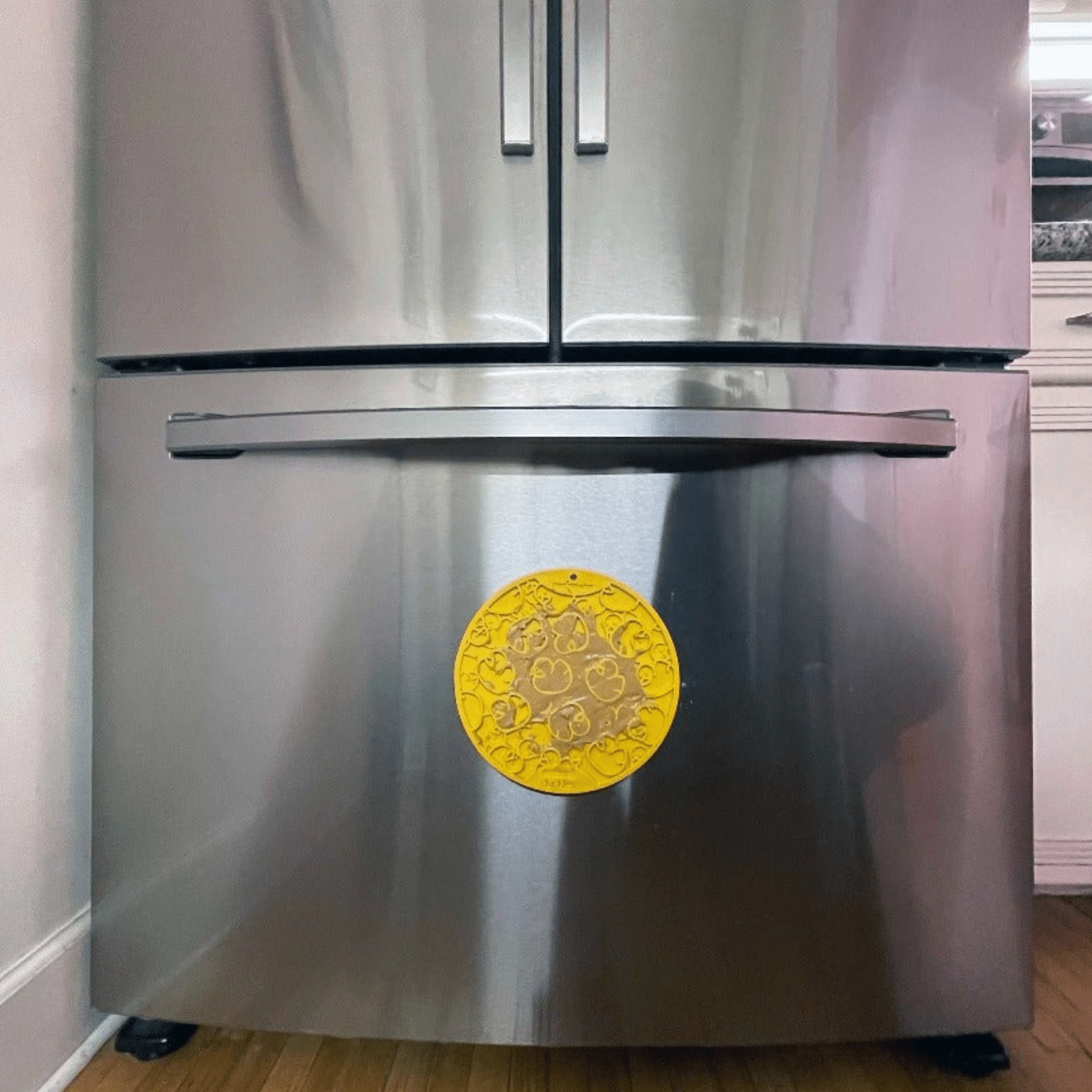 Yellow circular suction-cup dog lick mat attached to a stainless cabinet door