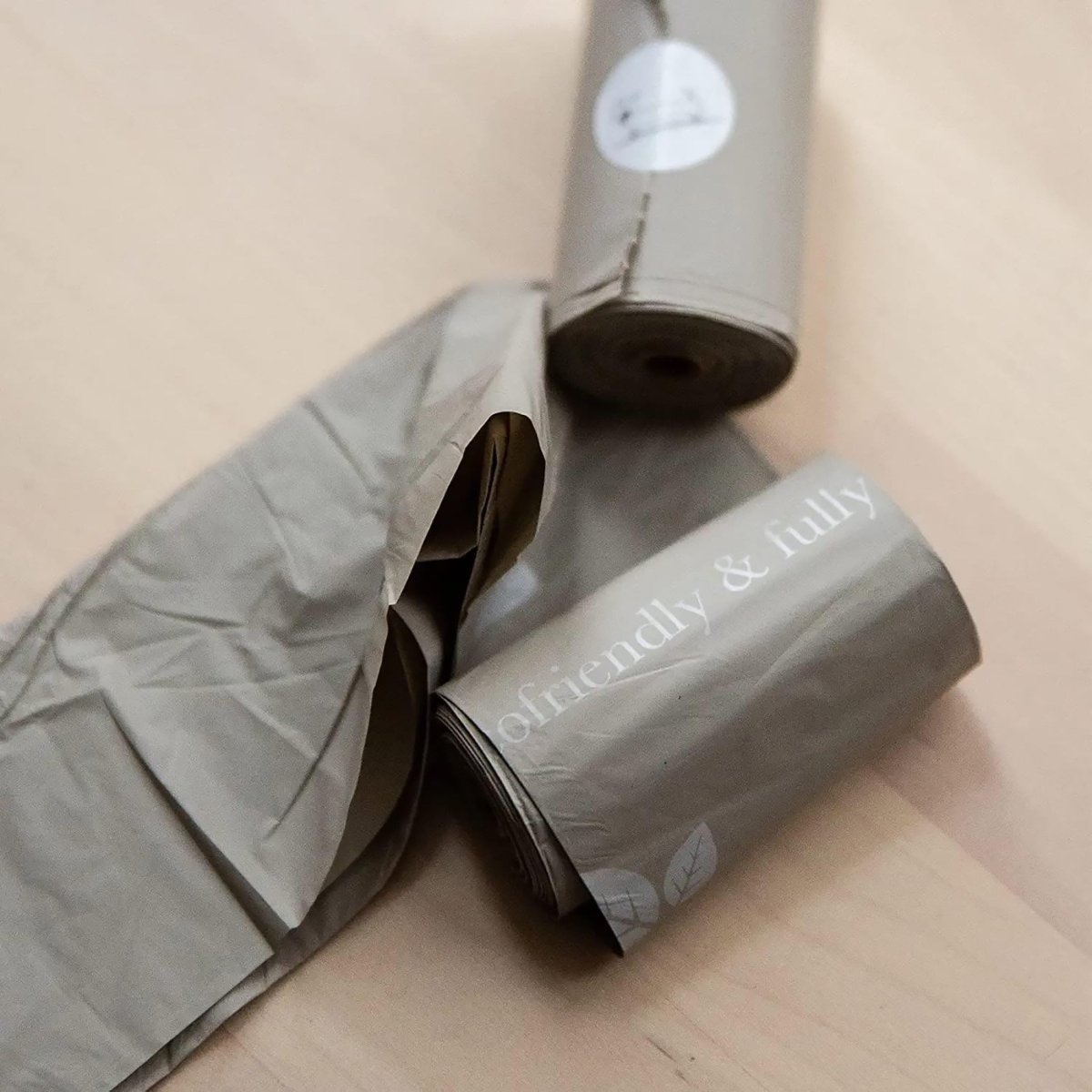 Dog waste bag roll with dispenser tag, pale gray bags unspooling from the roll