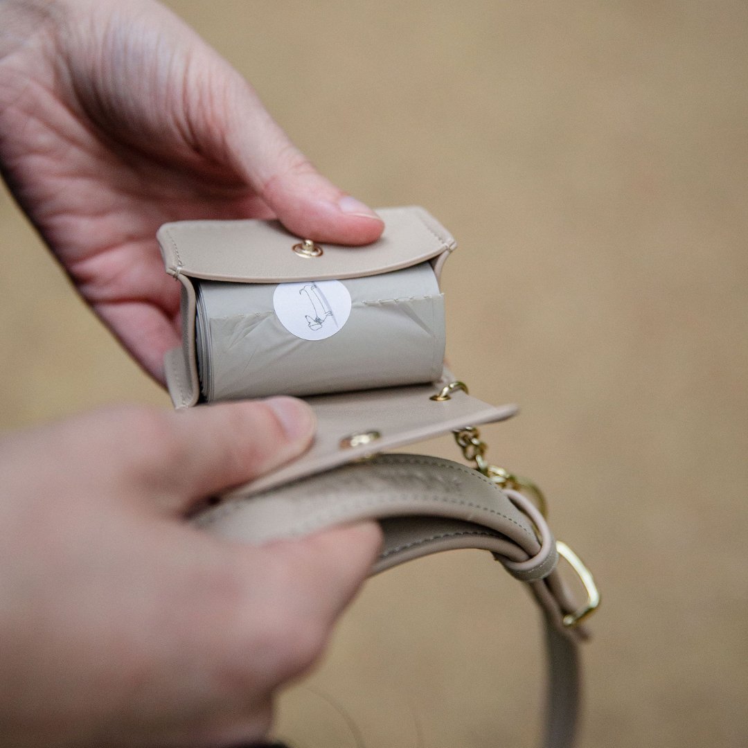 Dog waste bag dispenser pouch held in hand, gray roll visible inside the pouch