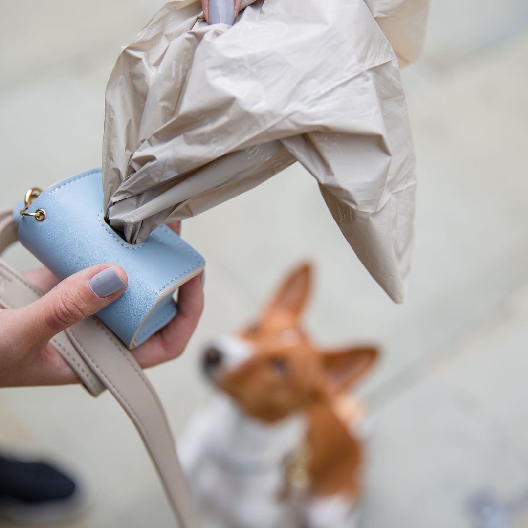 Dog waste bag dispenser pouch being filled, gray plastic bags coming out of the pouch
